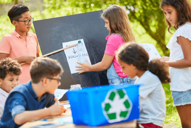 Middle school students gathered around a table and chalkboard brainstorming recycling projects for their school. Creatine moments of community through volunteer opportunities aids school retention efforts.